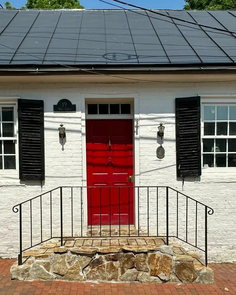 image of a white brick little house from early 1900s with a metal roof, black shutters, and red front door which is the home of Wildwood Psychotherapy in Leesburg, VA