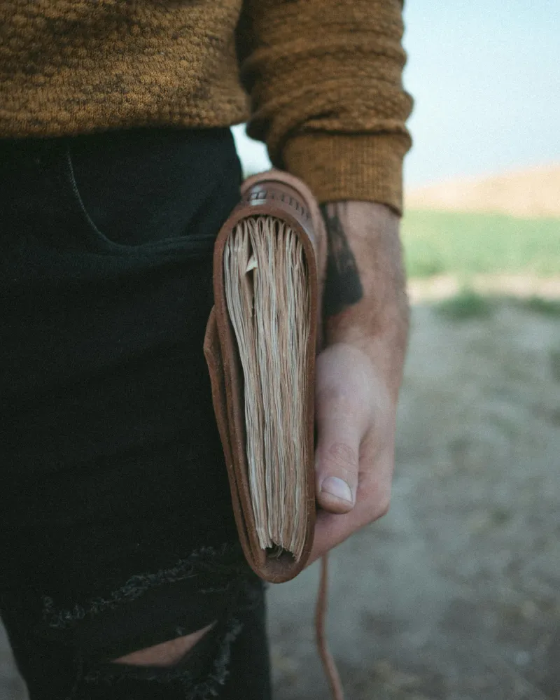 image of a man in a mustard sweater and black ripped jeans holding a leather-bound journal with hand-torn edges