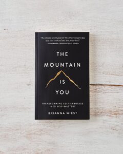 Book cover of Brianna Wiest's "The Mountain Is You" with black background, gold etched outline of a mountain peak at the center, and white font.